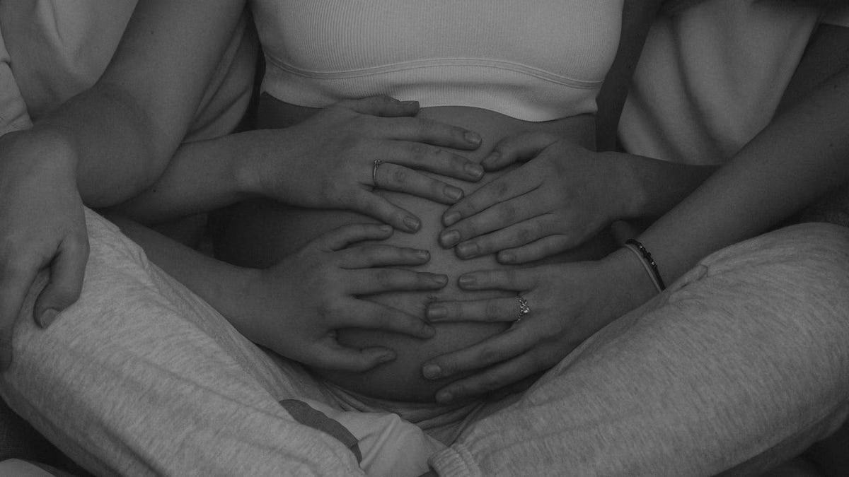 A close-up, grayscale photo of hands embracing a pregnant belly, symbolizing love and anticipation.